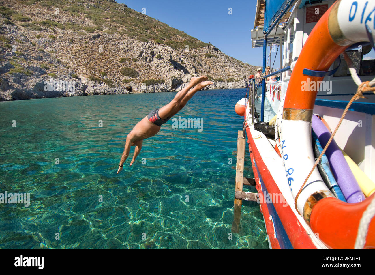 Un conciate l uomo nella sua 70s diving fuori da una barca nel Mar Egeo vicino l'isola greca di Symi o Simi Foto Stock