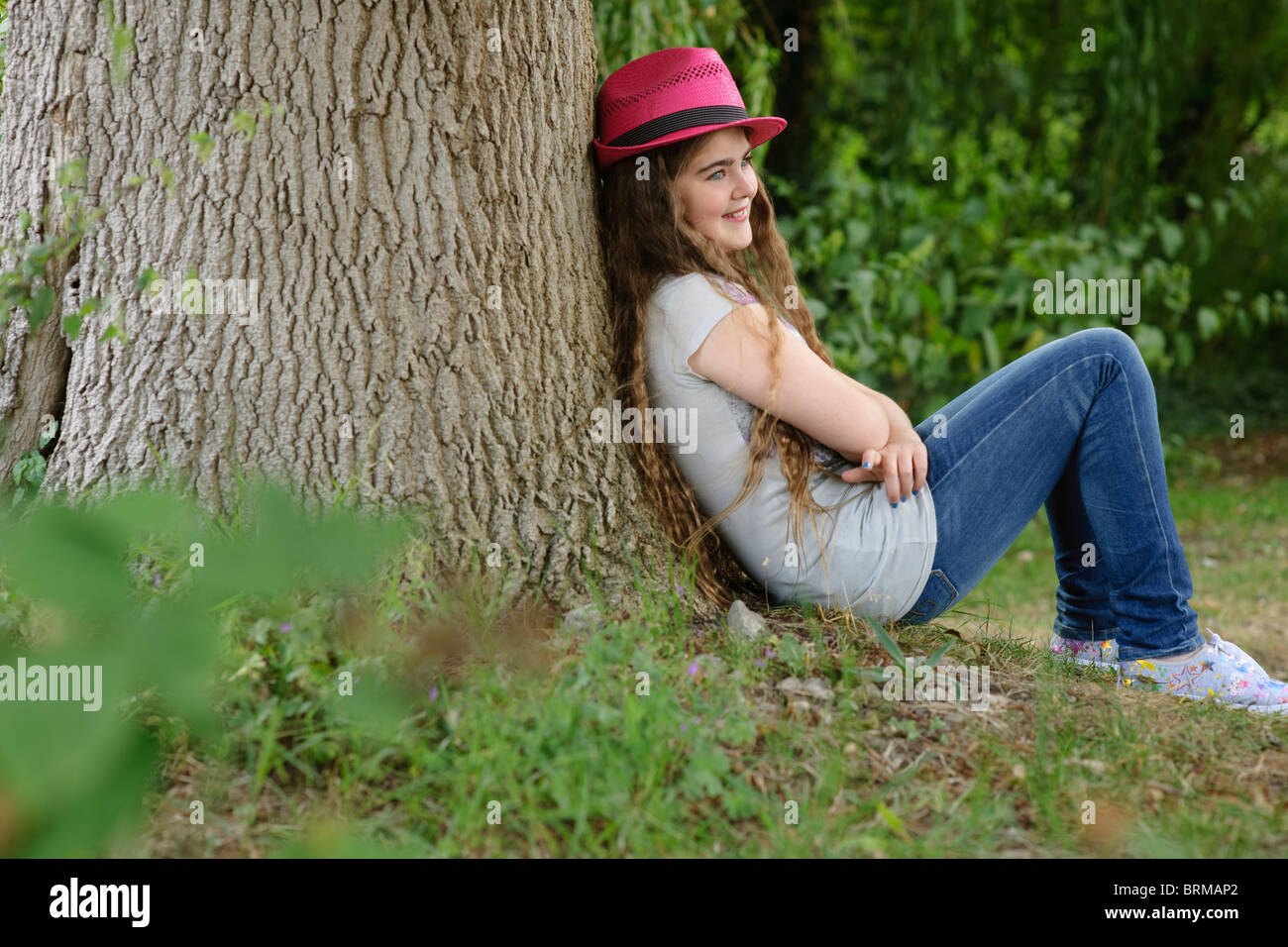 Ragazza in rosa hat seduti contro tree Foto Stock