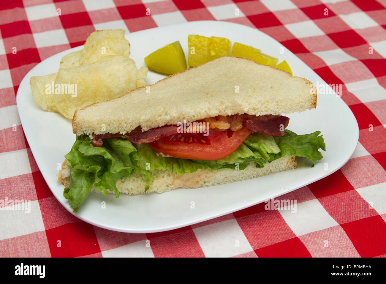 La metà di un sandwich blt su una piastra bianca con chip e sottaceti Foto Stock