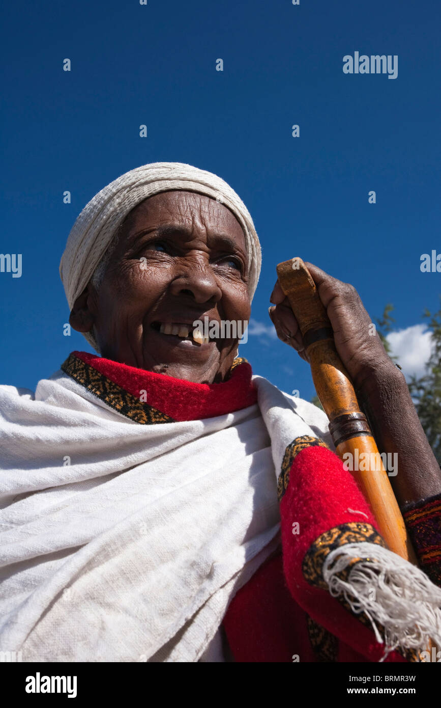 Ritratto di un sorridente donna anziana in un colorato abito tradizionale in appoggio la sua mano su un bastone da passeggio Foto Stock