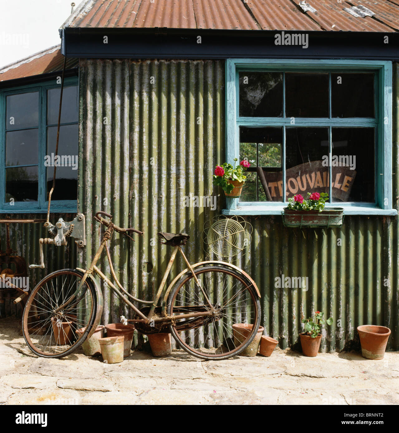 Vecchia bicicletta appoggiata contro la lamiera ondulata capannone con pale finestra blu Foto Stock