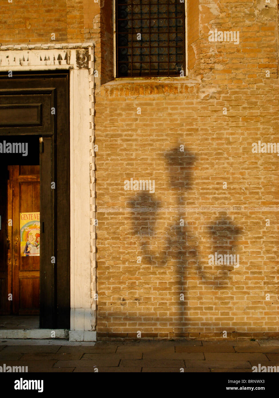 Silhouette della lampada contro un muro di mattoni con porta di legno, prese nel caldo sole di luce, in Campo Santo Stefano a Venezia, Italia Foto Stock