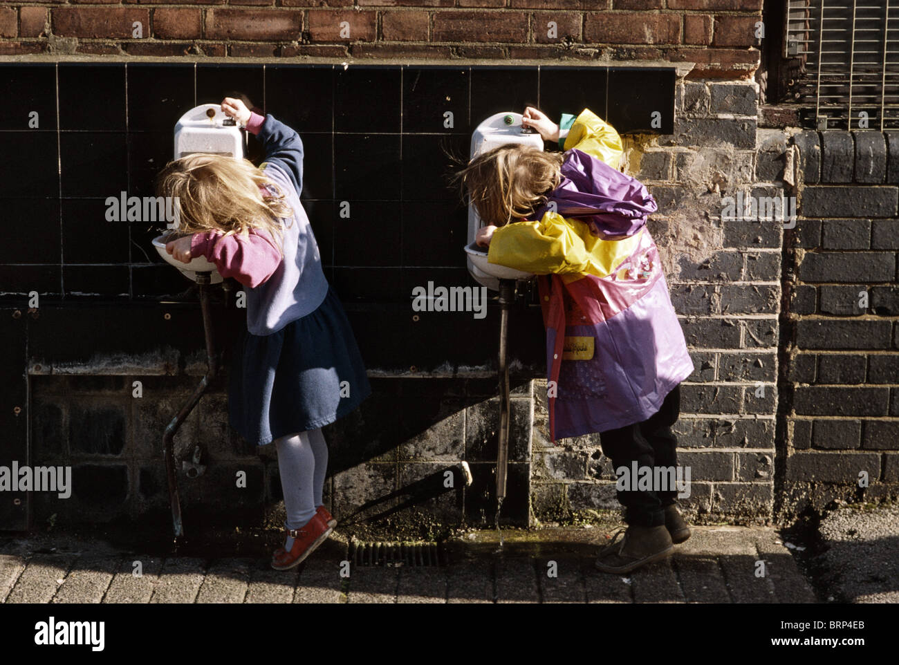 Due giovani ragazze per raggiungere la fontana di acqua potabile nella scuola di massa Foto Stock