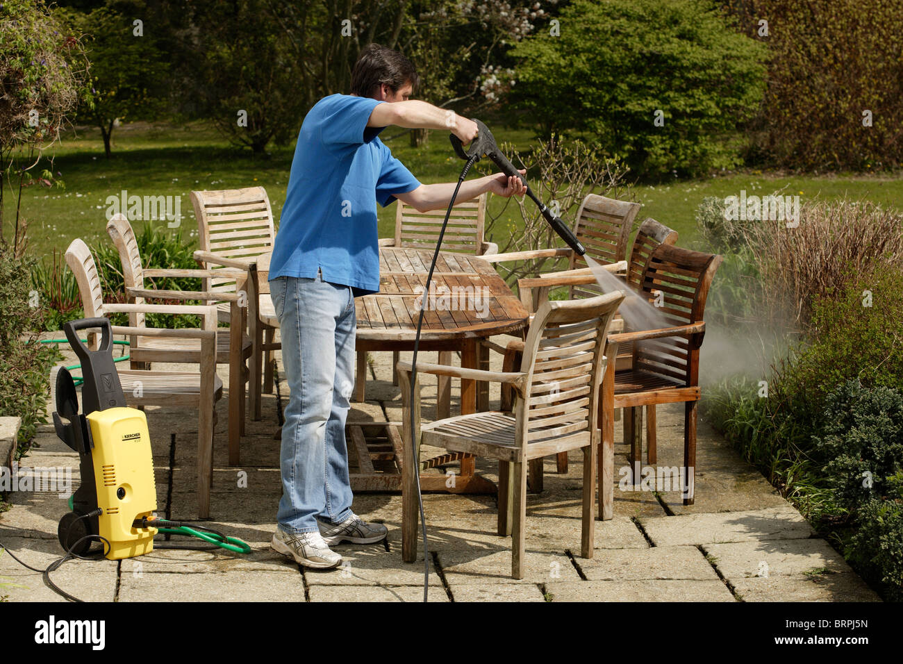 Uomo che utilizza un lavaggio a pressione per pulire legno teak mobili da  giardino Foto stock - Alamy
