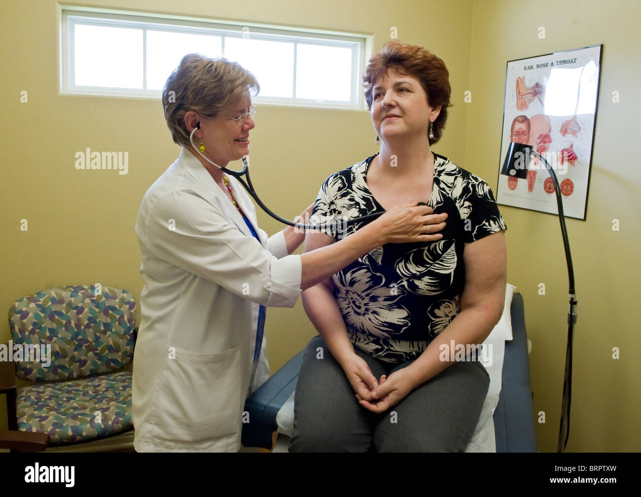 Femmina di infermiera utilizza uno stetoscopio per ascoltare femmina femmina paziente 's cuore durante la visita di office nella sala esame Foto Stock