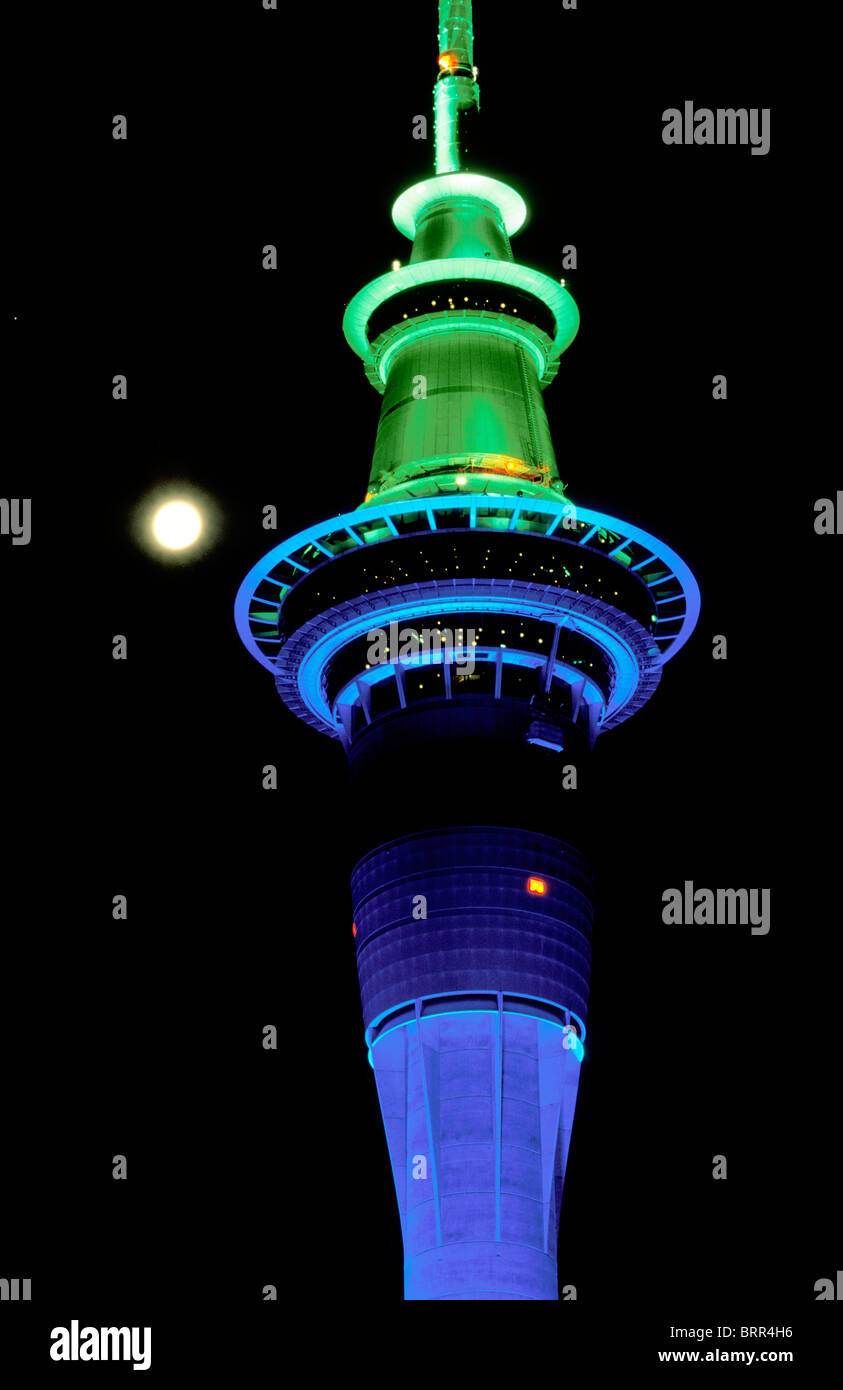 La Sky Tower di Auckland torre illuminata in blu e verde di notte visto contro una luna piena Foto Stock