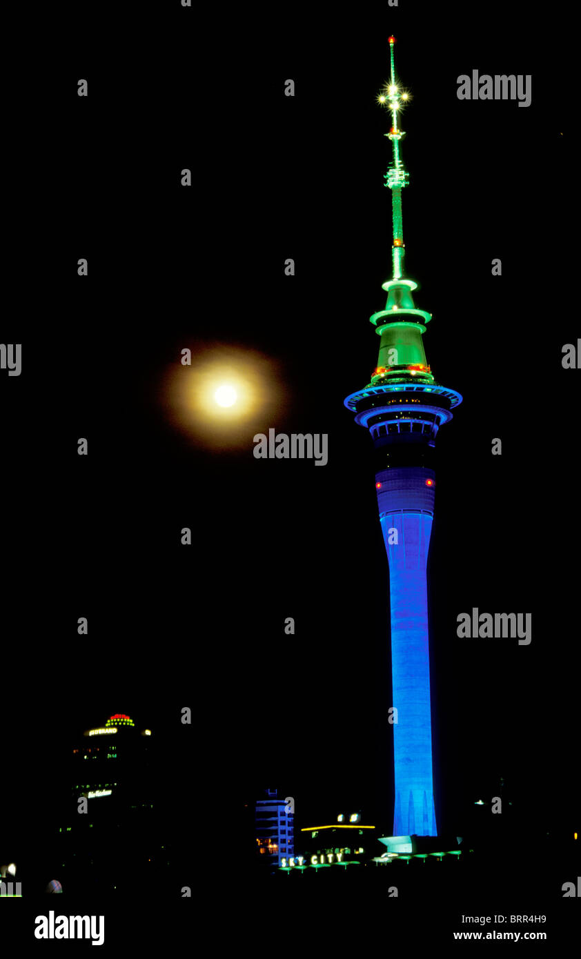 La Sky Tower di Auckland illuminato in blu e verde di notte visto contro una luna piena Foto Stock
