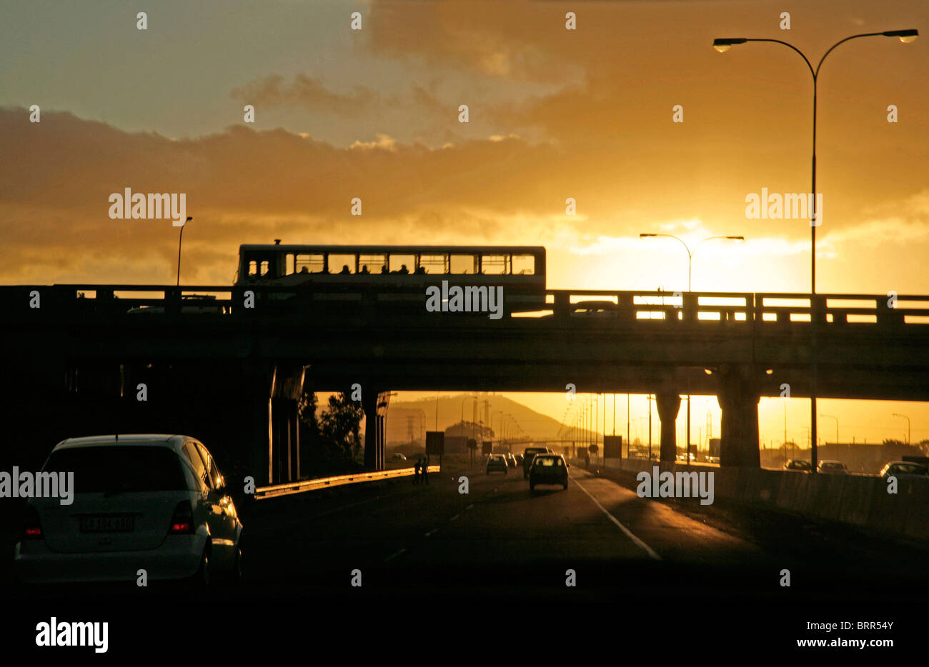 Il traffico su autostrada e un bus su un cavalcavia stagliano al tramonto Foto Stock