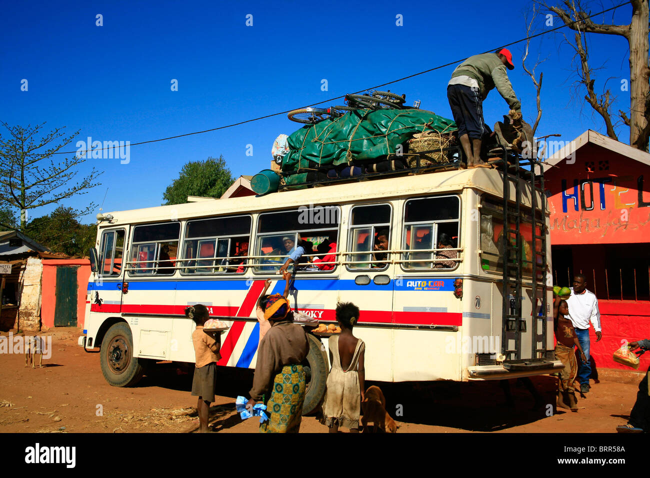 Venditori ambulanti che vendono merci di passeggeri di un autobus mentre un uomo carichi di bagagli sul tetto. Foto Stock