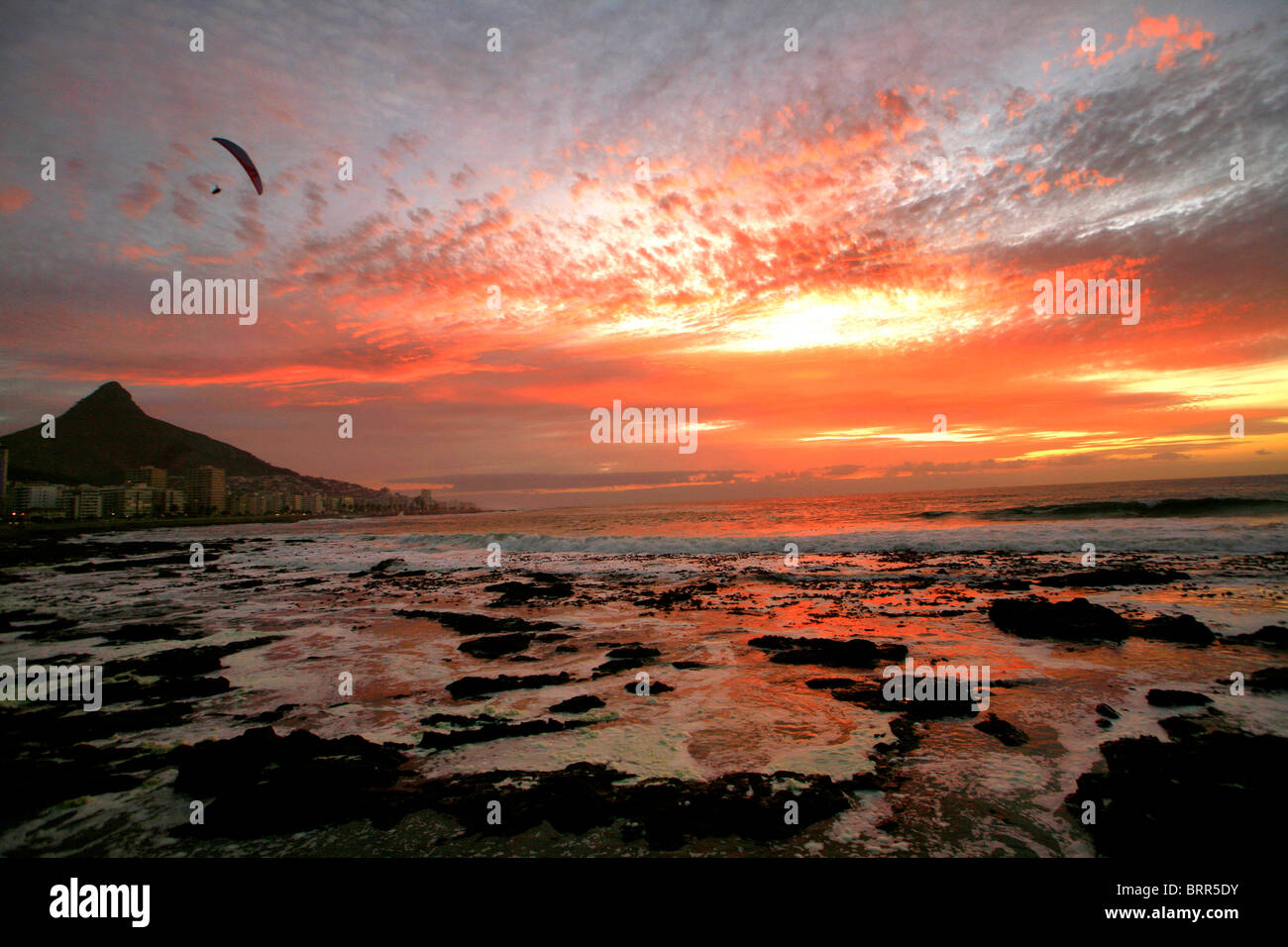Moody vista sul mare punto anteriore sulla spiaggia al tramonto, con drammatica nuvole e un parapendio soaring sull Oceano Atlantico Foto Stock