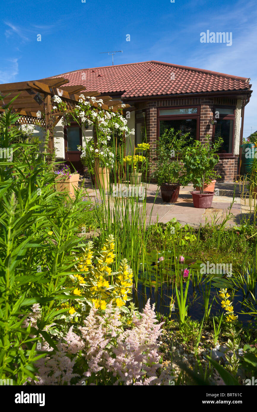 Giardino sul retro di bungalow affacciato sul laghetto con pergola e patio, Inghilterra Foto Stock