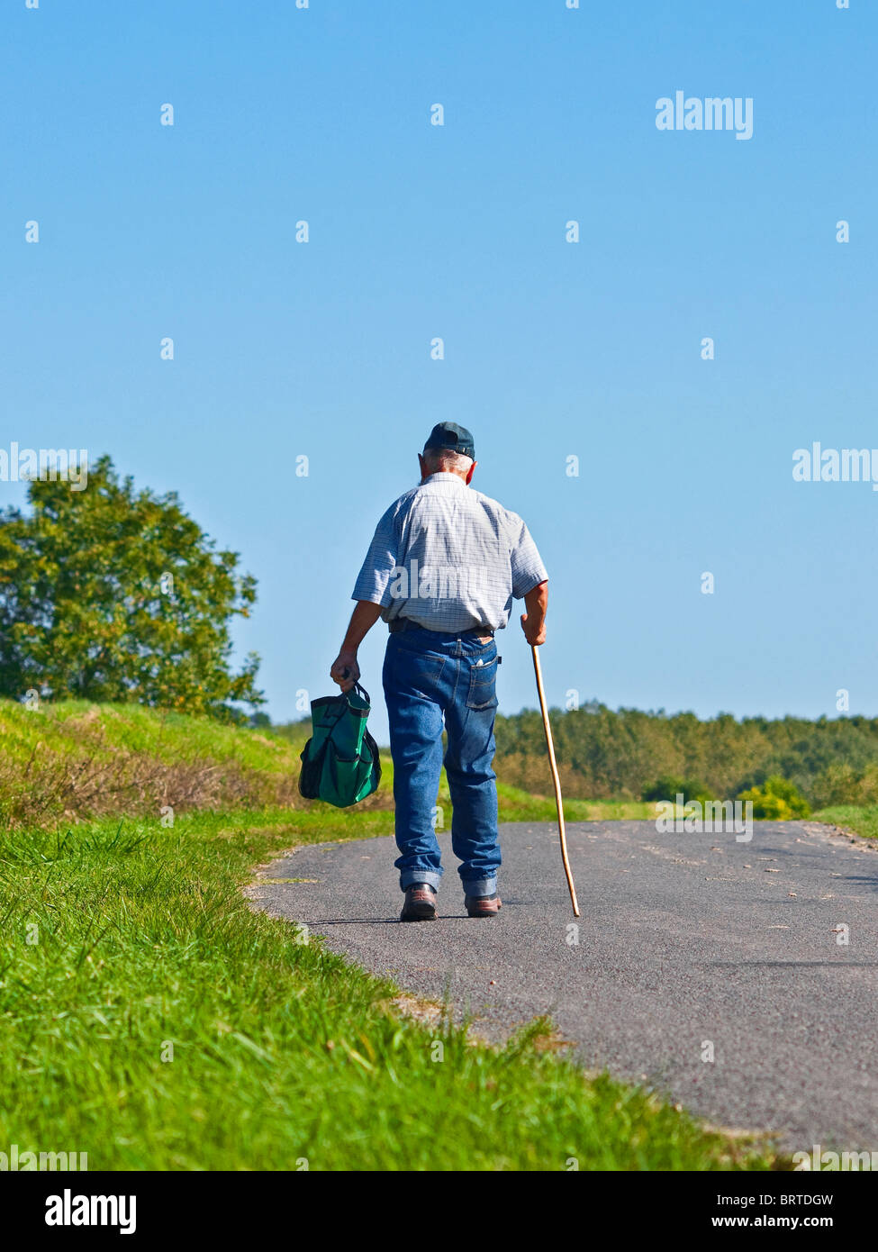 Uomo vecchio con bastone a piedi lungo la strada di campagna - Indre-et-Loire, Francia. Foto Stock