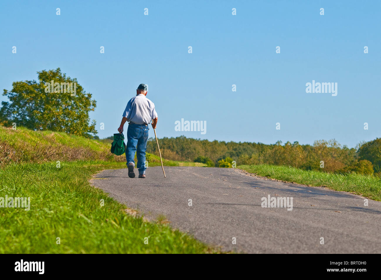 Uomo vecchio con bastone a piedi lungo la strada di campagna - Indre-et-Loire, Francia. Foto Stock