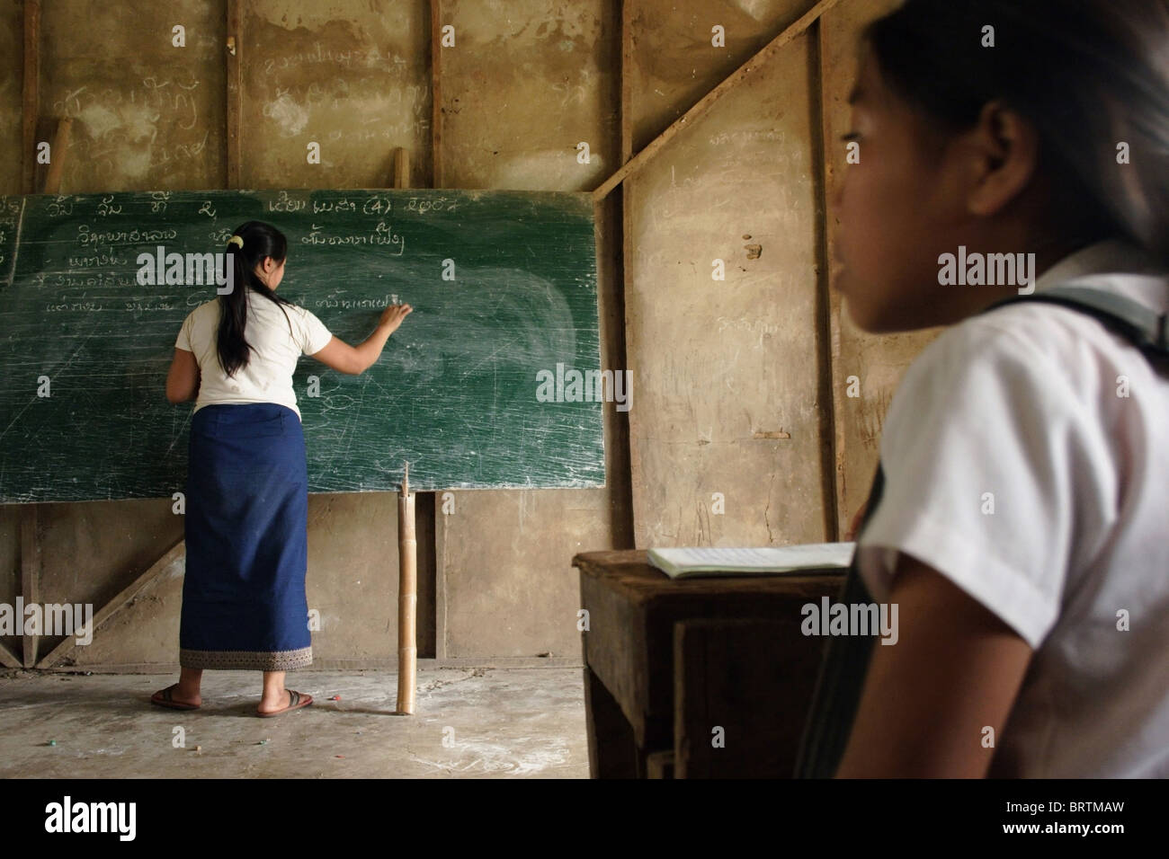 Un insegnante è la scrittura di note sulla lavagna verde come una ragazza studente studi presso una scuola primaria di Ban Buamlao, Laos. Foto Stock