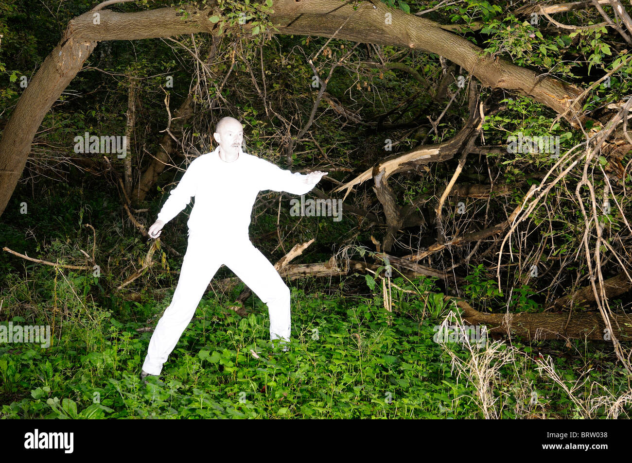 Alien uomo in bianco luminoso con vestiti catturati in una fitta foresta infestata da erbacce Foto Stock