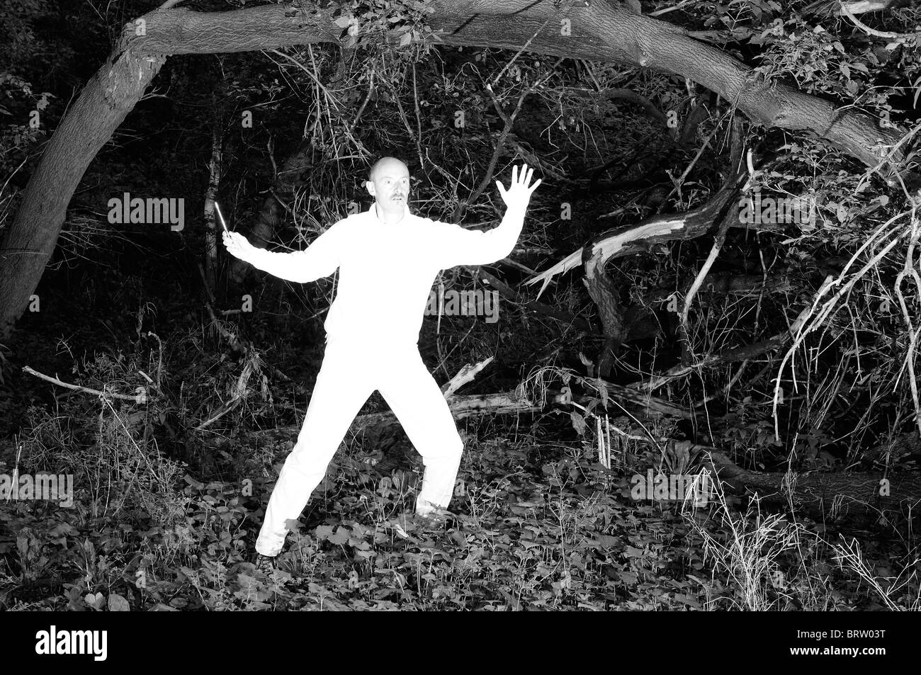 Alien uomo in bianco puro con dispositivo elettronico sorpreso in una fitta foresta monocromatico Foto Stock