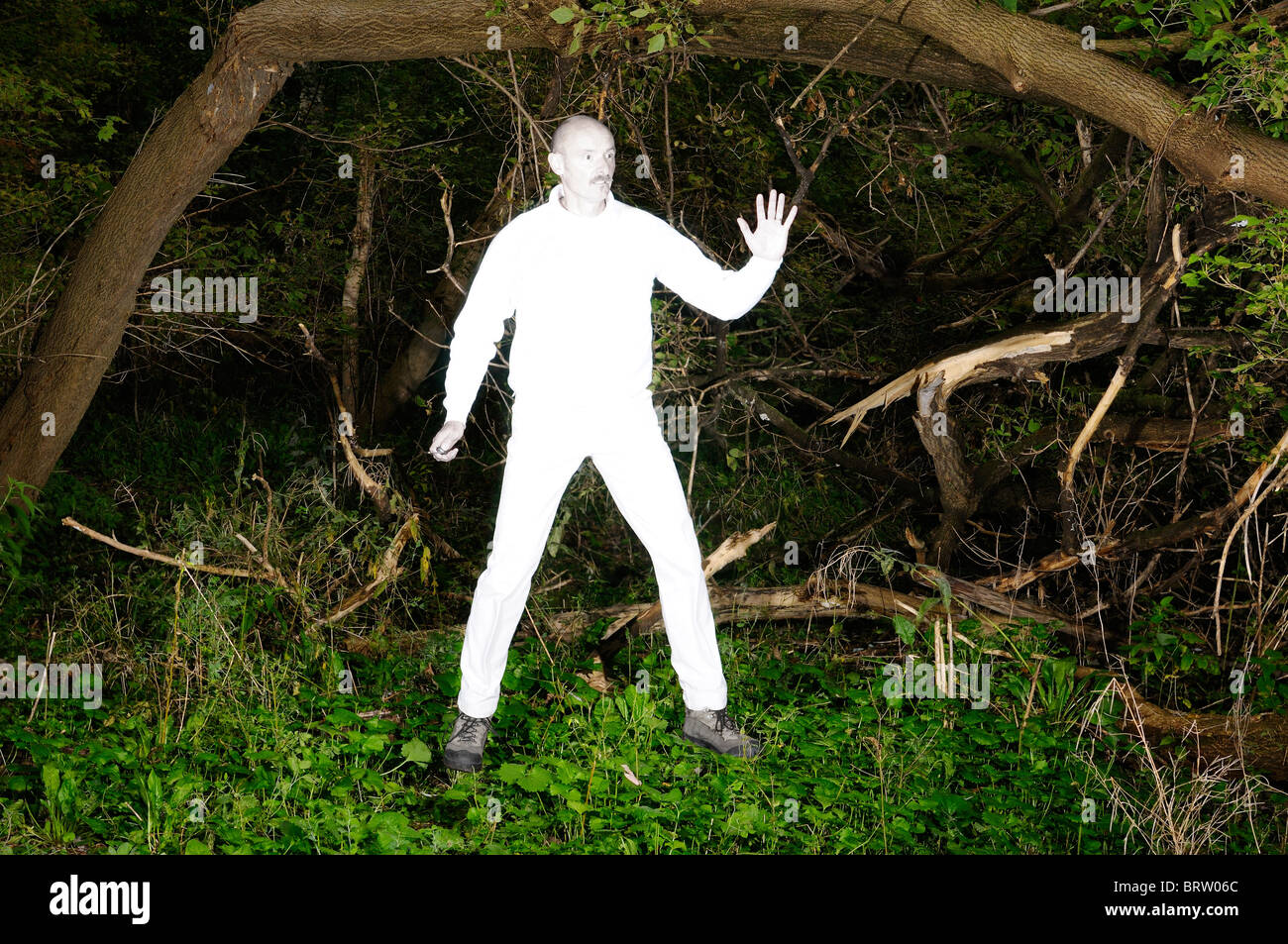 Floating alien uomo in bianco luminoso con vestiti catturati in una fitta foresta infestata da erbacce Foto Stock