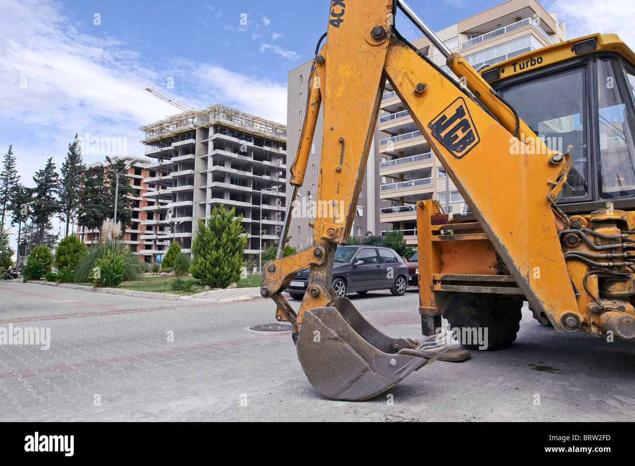 L'artiglio di un giallo JCB digger poggia sulla strada di fronte ad un appartamento sito di sviluppo. Foto Stock