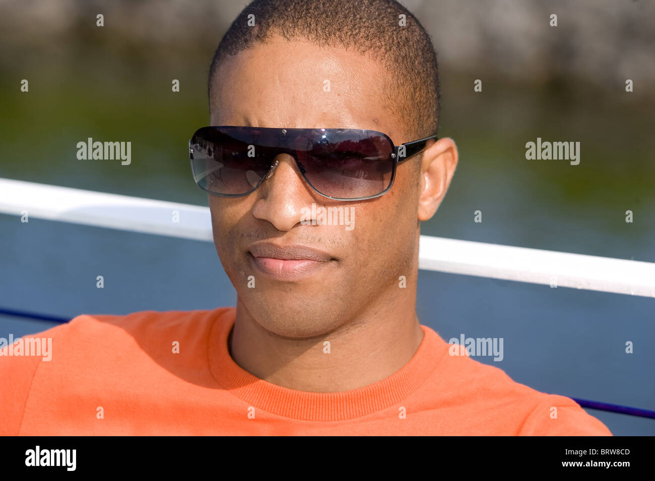 Un giovane americano africano uomo seduto vicino all'acqua con gli occhiali da sole sul cercando gravi Foto Stock