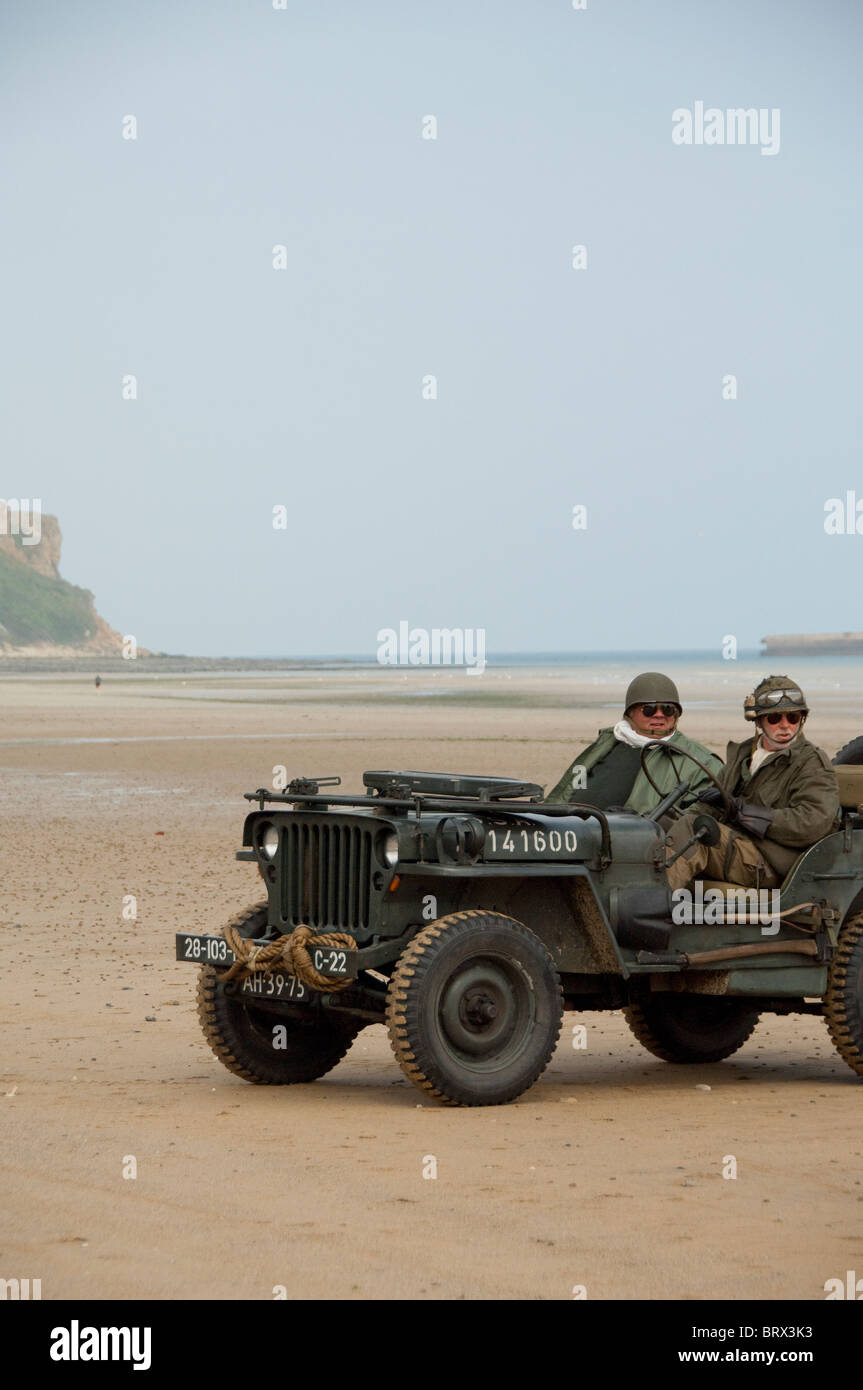 Francia, Normandia, Arromanches. Vintage jeep con i soldati in uniforme guida su storico campo di battaglia. Foto Stock