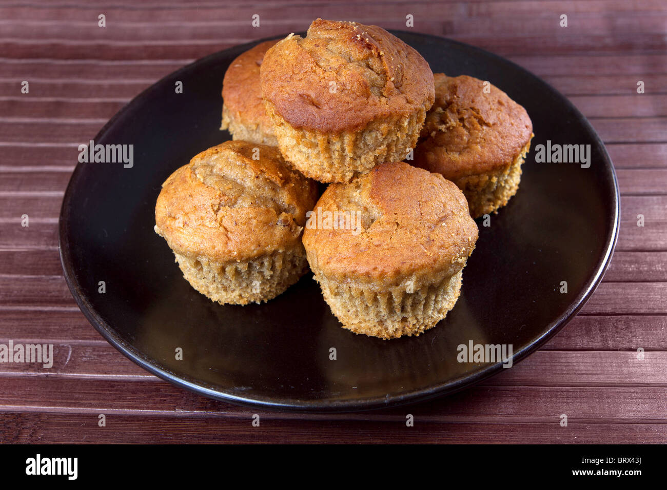 Piccola pila di cinque muffin alla banana in giallo su una piastra nera su uno sfondo di legno Foto Stock