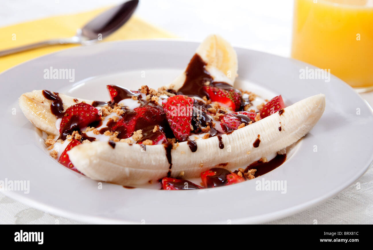 Una piastra di sani di banana split con yogurt, fragole e a basso contenuto di grassi al cioccolato caldo topping Foto Stock