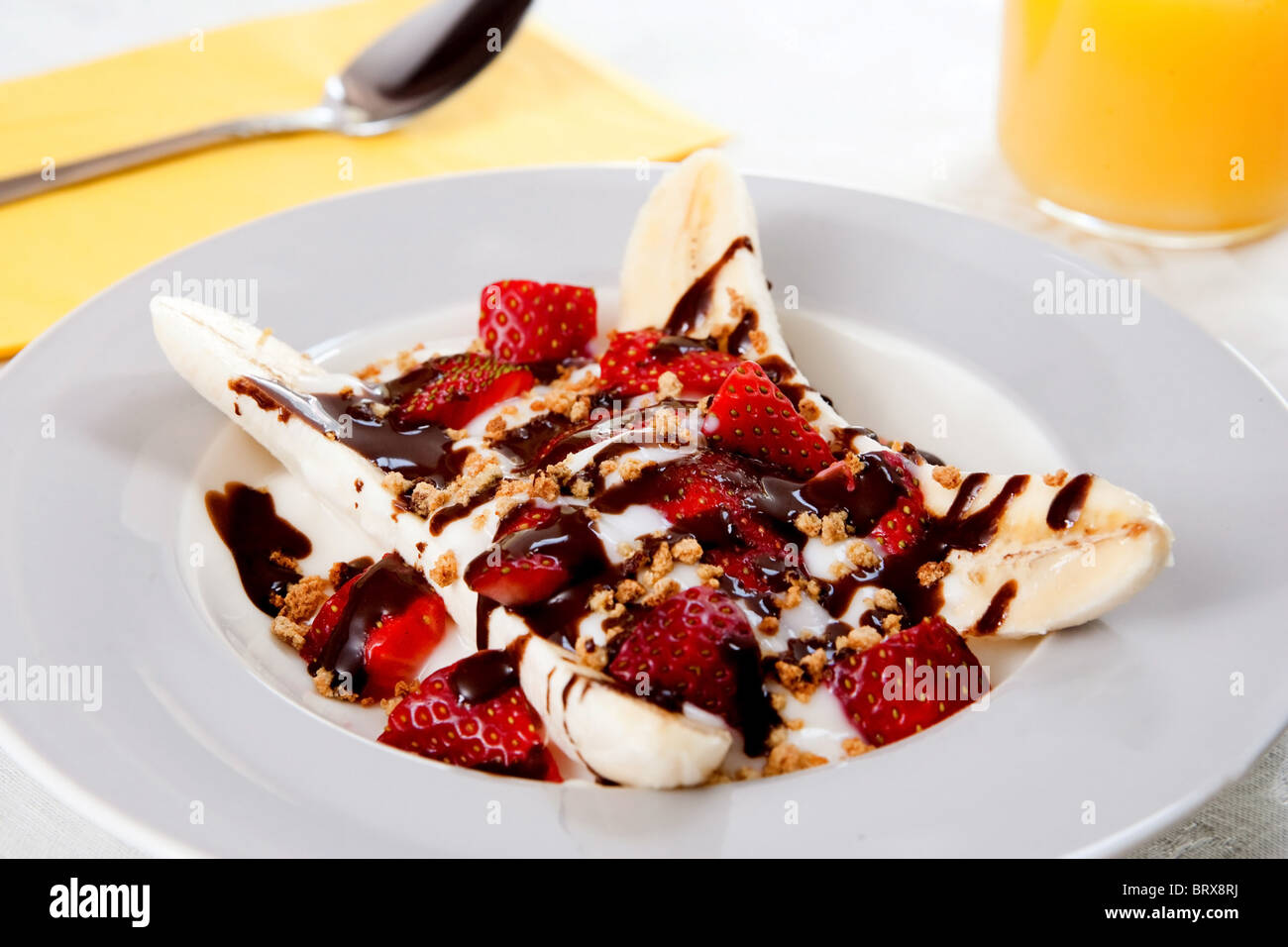 Una piastra di sani di banana split con yogurt, fragole e a basso contenuto di grassi al cioccolato caldo topping Foto Stock