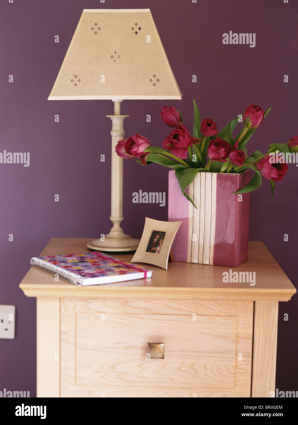Close-up di lampada e rose in contenitore di malva sul comodino in camera da letto viola Foto Stock