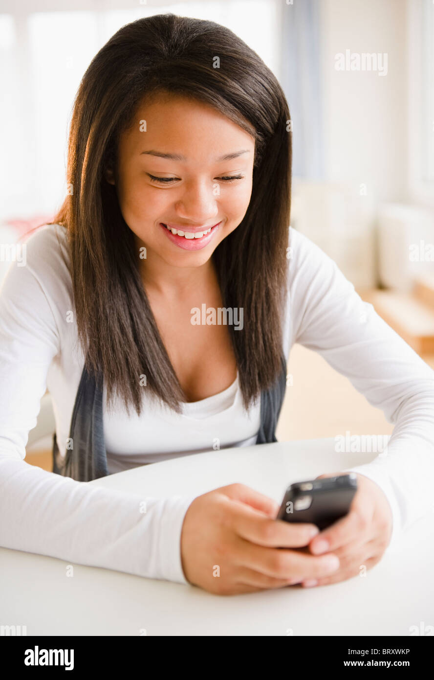 Sorridente razza mista ragazza adolescente di messaggistica di testo sul telefono cellulare Foto Stock