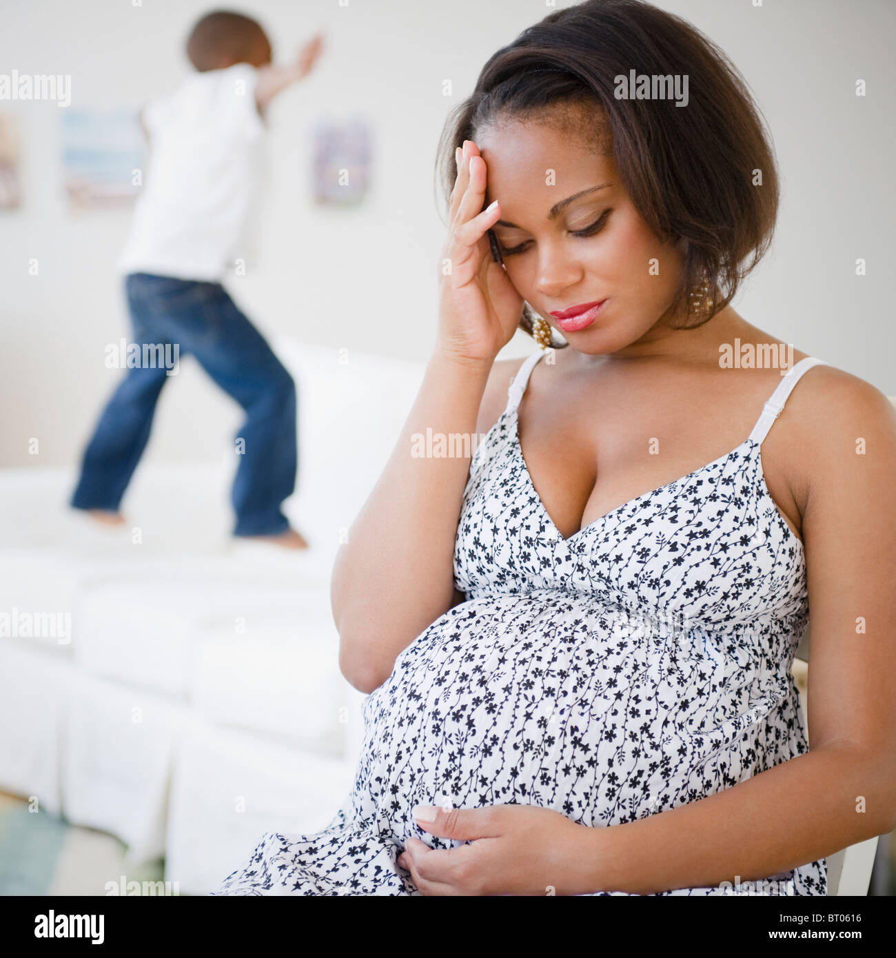 Gravidanza madre nera seduta con testa in mani mentre figlio salta sul letto Foto Stock