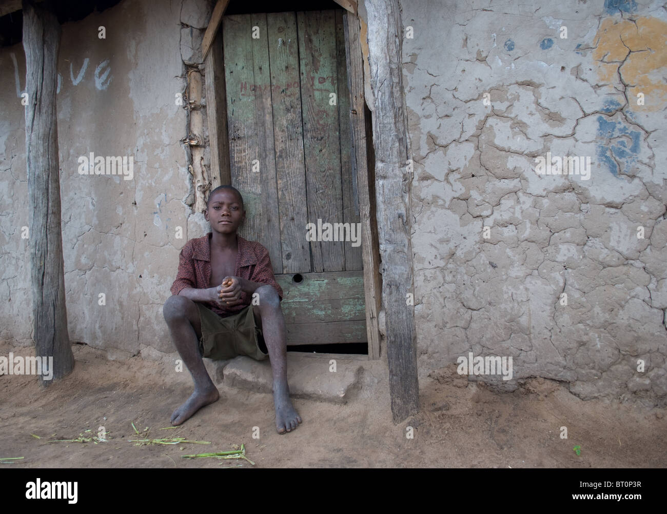 Ritratto di un ragazzo adolescente seduto fuori casa sua nel villaggio dello Zambia. Foto Stock