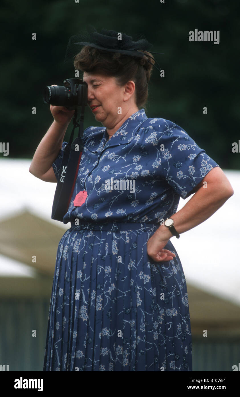 Donna di prendere una fotografia o guardando attraverso la fotocamera con un lato posizionato saldamente sul suo hip Foto Stock