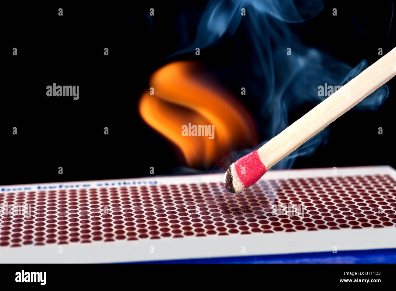 Un luci matchstick dopo che si è battuto contro la pietrina superficie di una scatola di confronto. Foto Stock