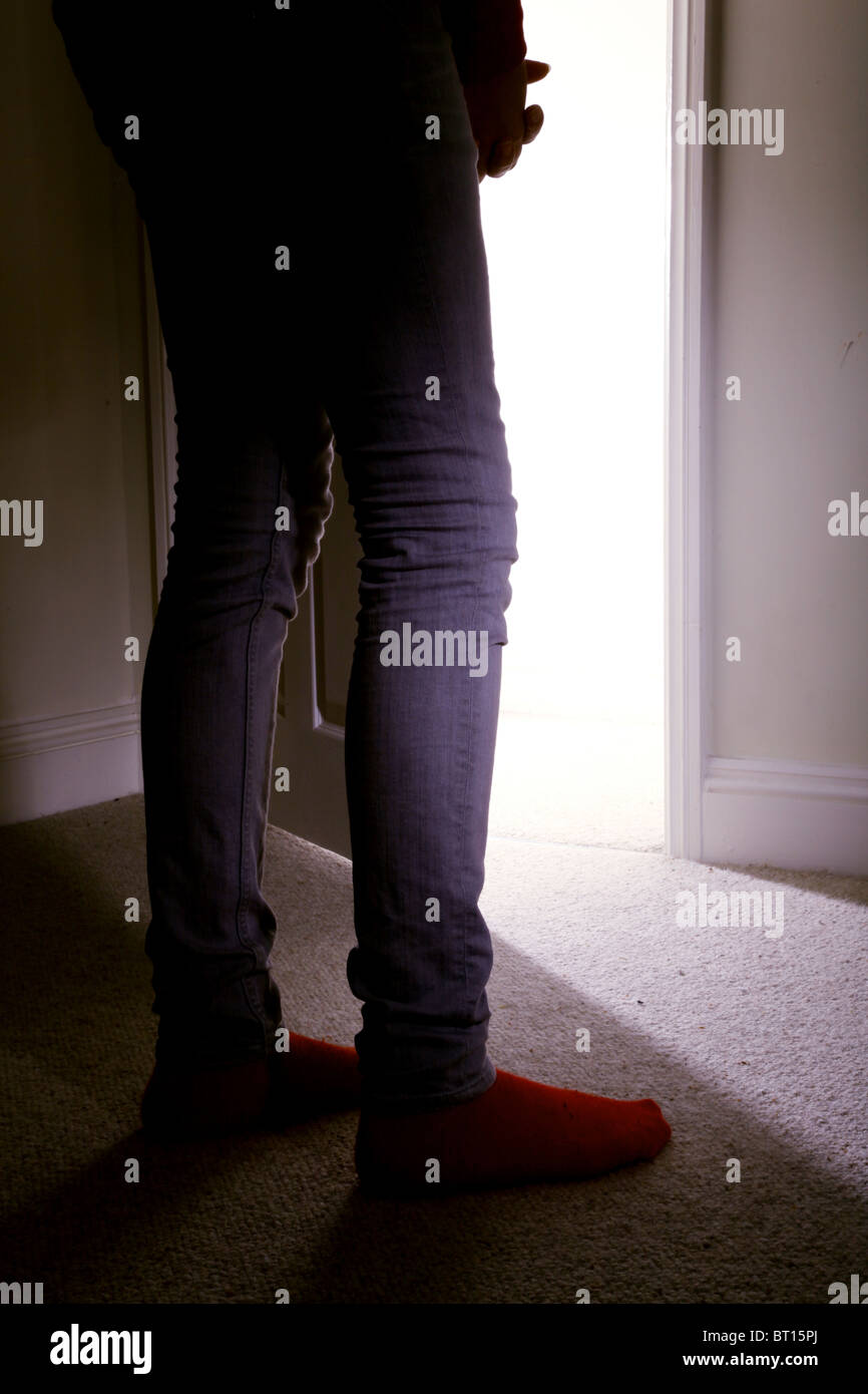 Giovane ragazza in piedi in una stanza buia rivolta verso una porta aperta. Foto Stock