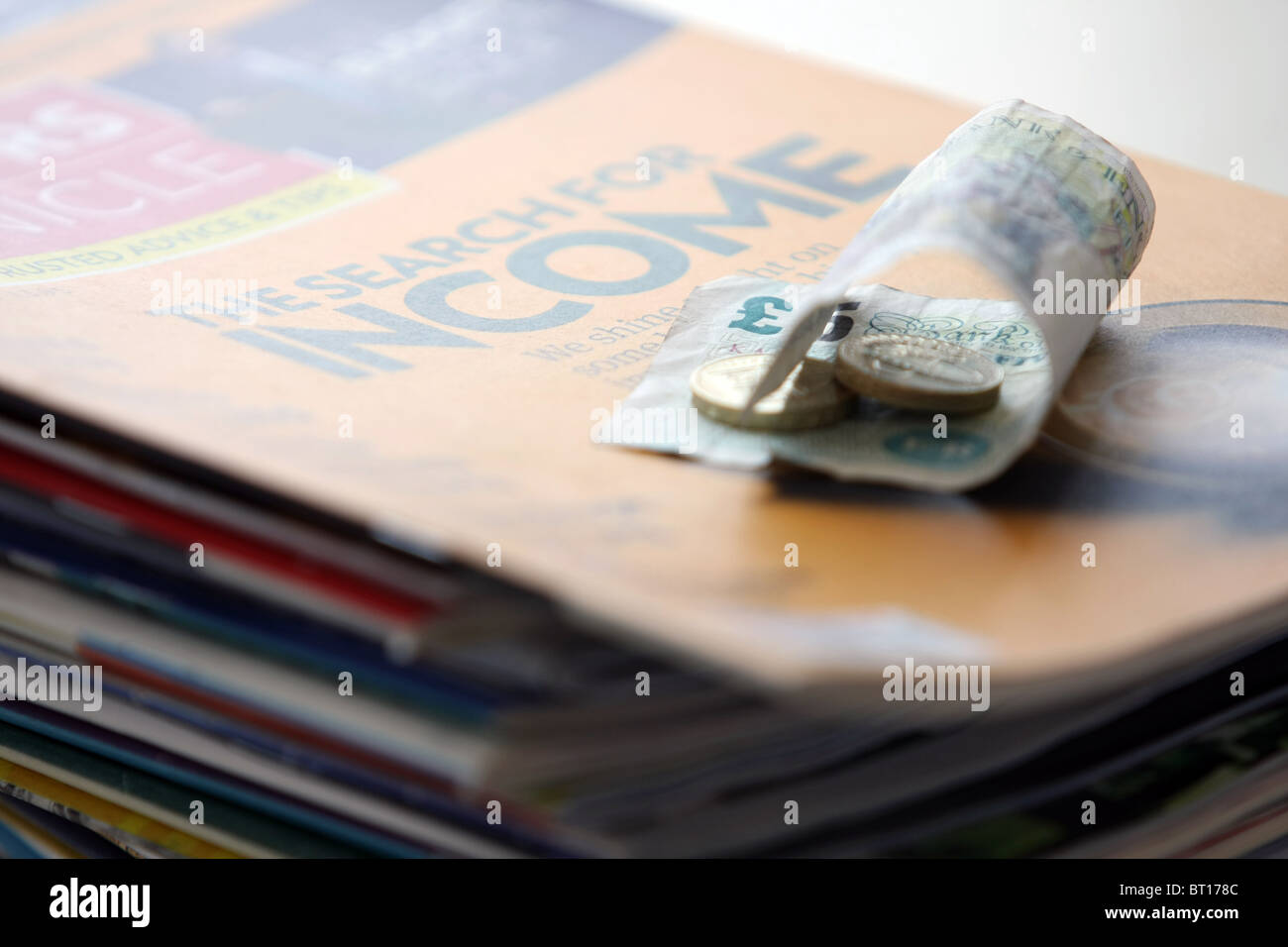 Una sterlina £ 5 nota e due £1 monete su una pila di riviste finanziarie Foto Stock