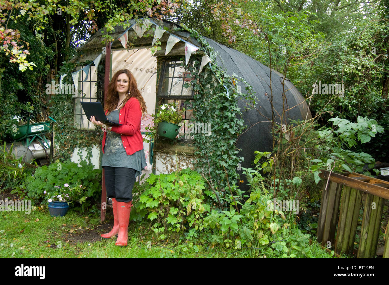 Woman in Red wellies al di fuori del suo ufficio di casa a un convertito WWII bomb shelter nel suo giardino sul retro. Foto Stock