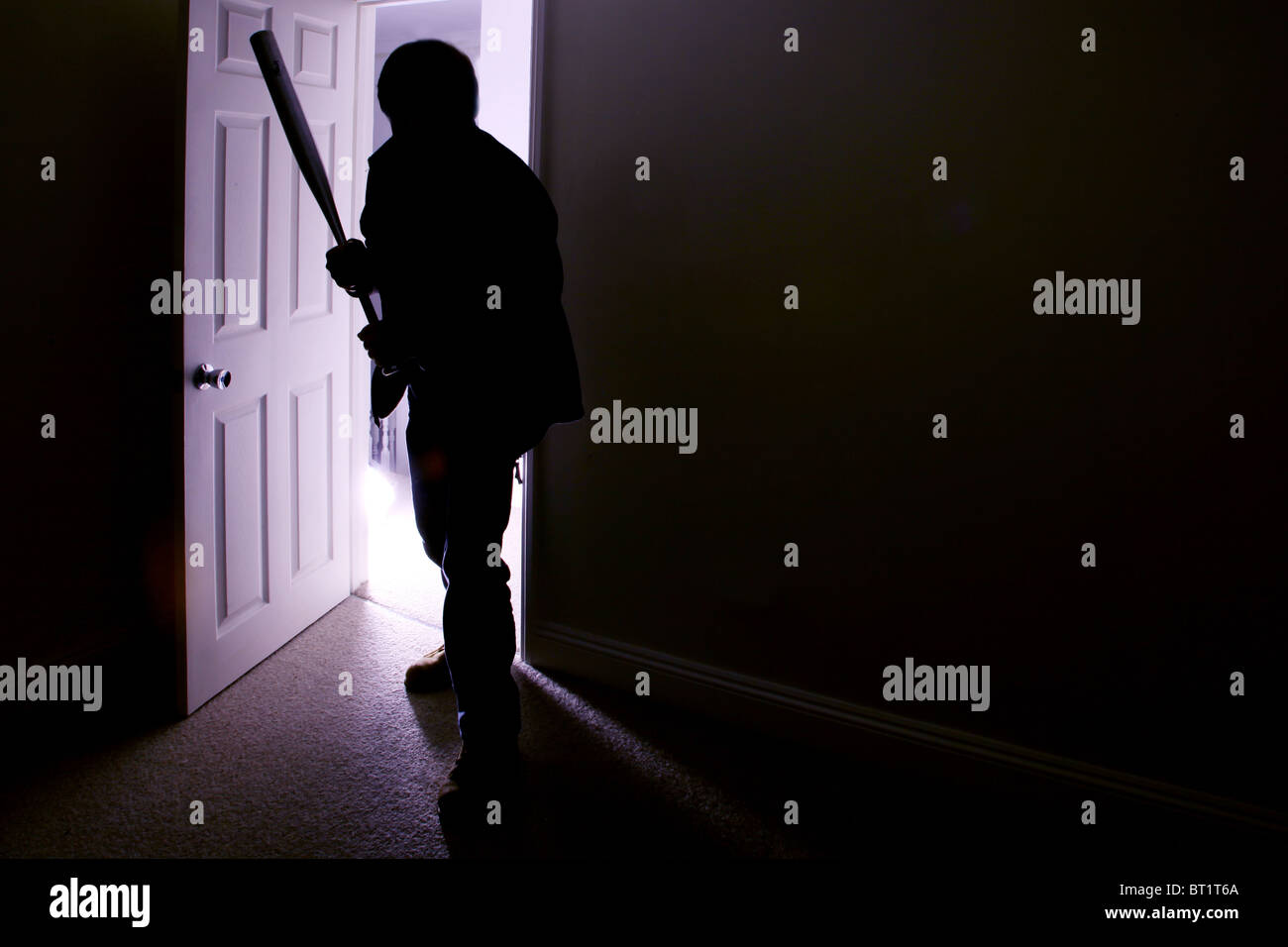 Silhouette di un maschio con una mazza da baseball di entrare in una stanza buia Foto Stock