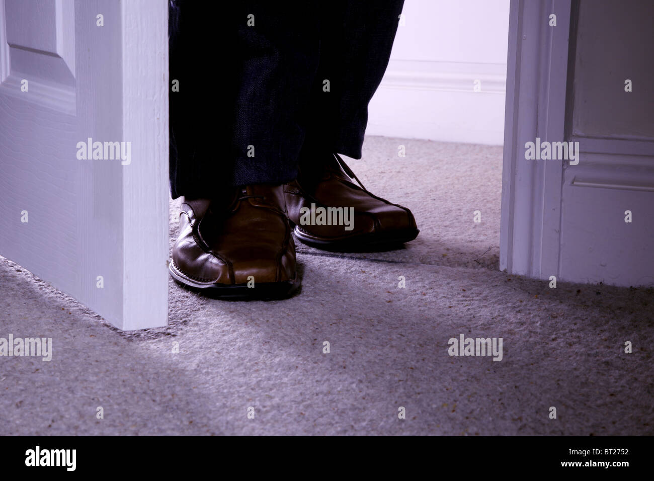 Uomo in piedi al di fuori di una porta aperta, piedi soltanto. Foto Stock