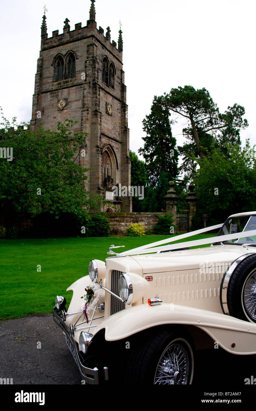 Un matrimonio classico auto è parcheggiata fuori una gotica chiesa Inglese in campagna. Foto Stock