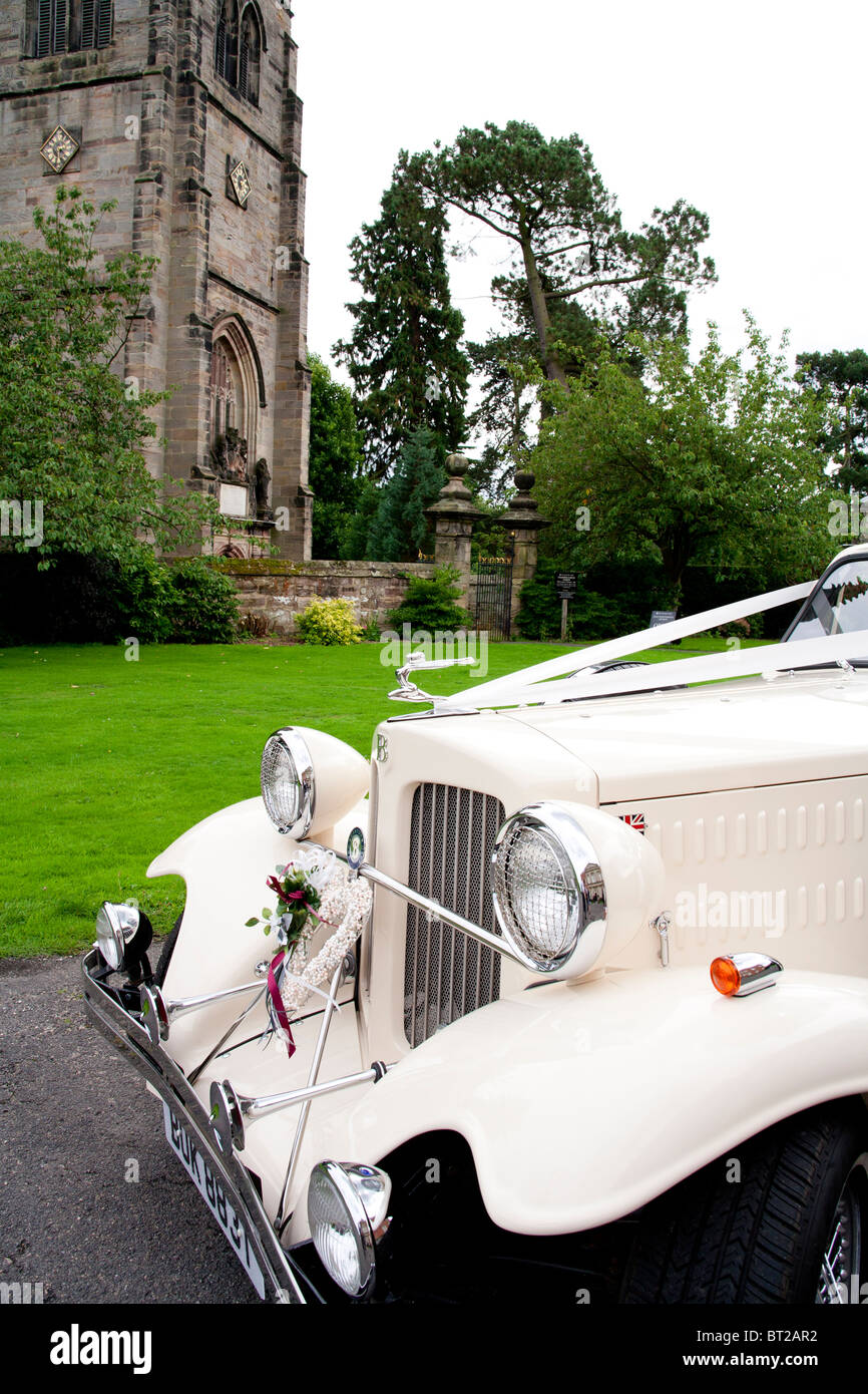 Un matrimonio classico auto è parcheggiata fuori una gotica chiesa Inglese in campagna. Foto Stock
