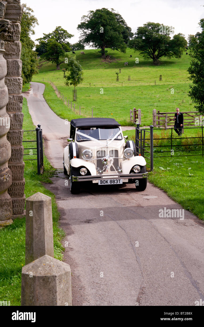 Un classico bianco auto nozze entra nel terreno di un inglese maestosa casa per un matrimonio. Foto Stock