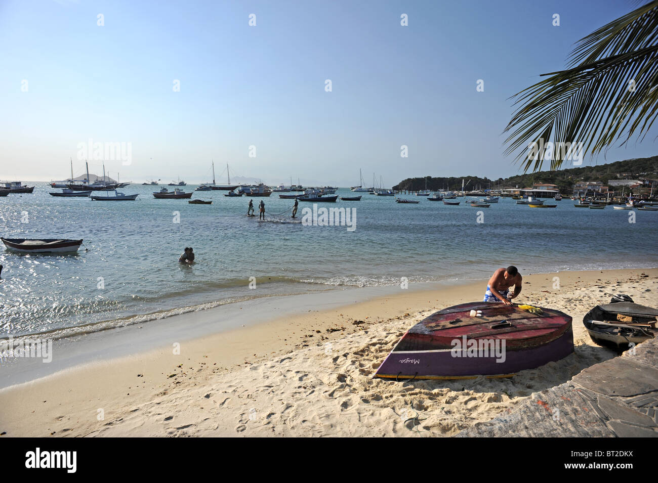 Un uomo che ripara la sua barca sulla spiaggia di Canto Buzios Foto Stock