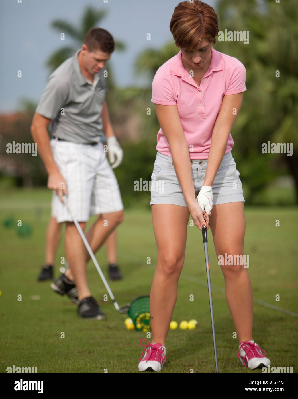 Giocatore di golf femminile sulla gamma di guida. Un golfista maschio in background. Foto Stock