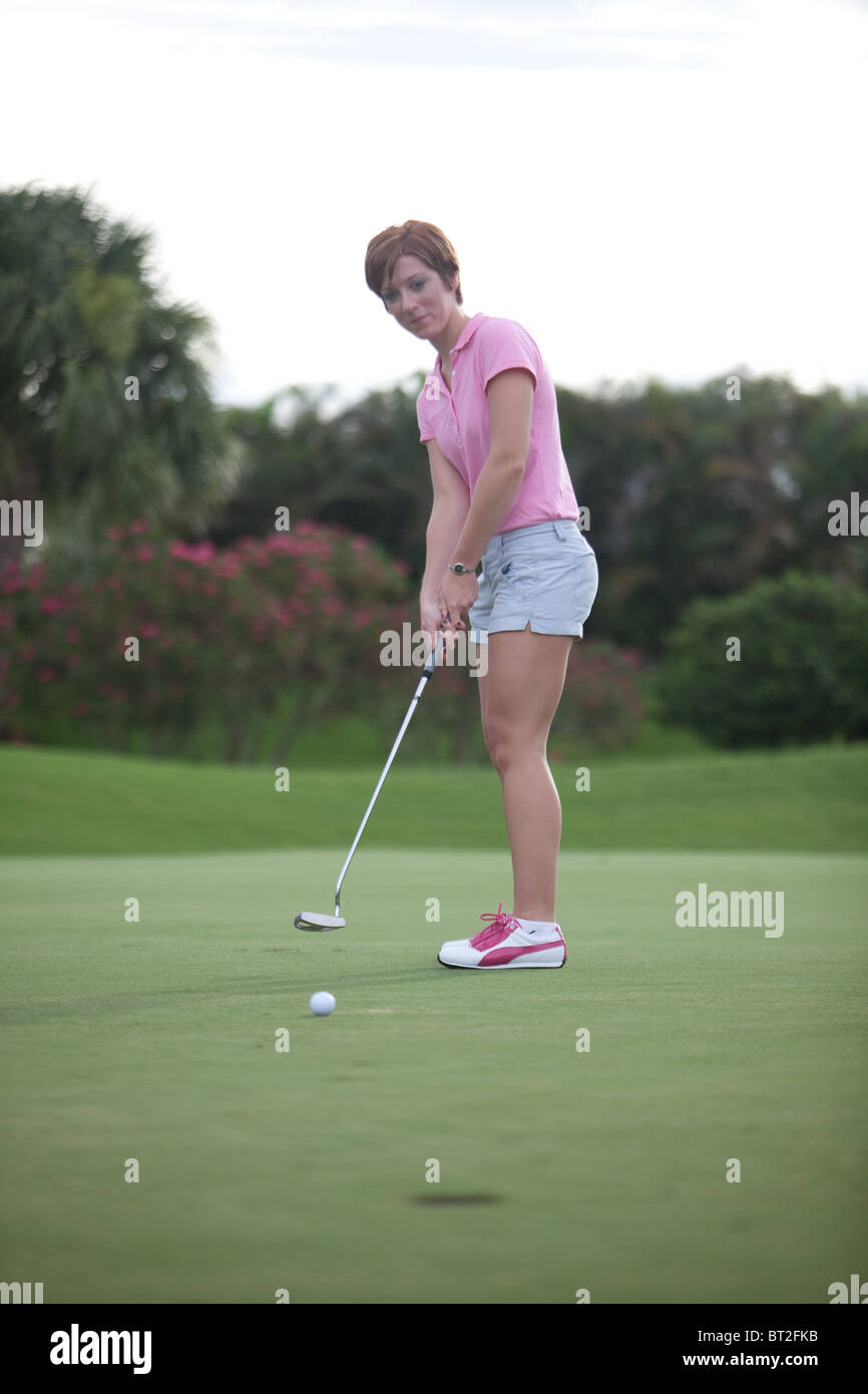 Giocatore di golf femminile mettendo, indossa una camicia rosa Foto Stock