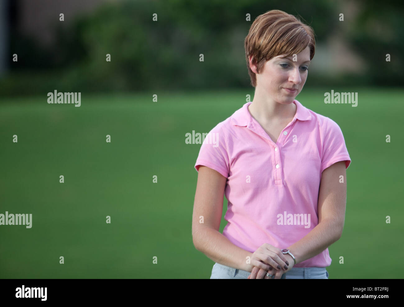 Signora giovane (femmina golfista) con corti capelli biondi e indossa una maglia rosa shirt attende il suo giro Foto Stock