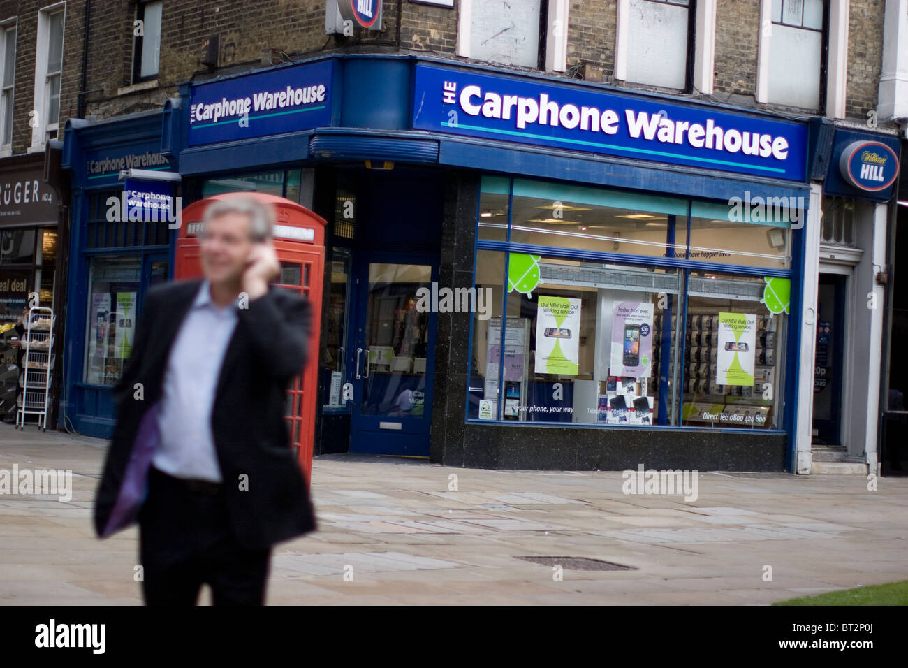 Un negozio di telefonia mobile Carphone Warehouse a Moorgate, Londra, Regno Unito, con un membro del pubblico al telefono davanti a una classica cabina telefonica rossa Foto Stock