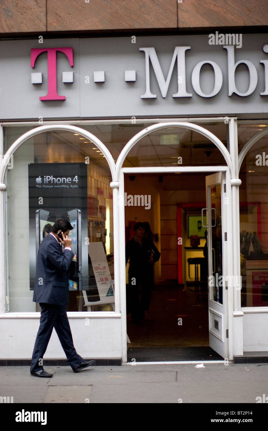 Uomo al telefono cellulare che passa accanto a un punto vendita T-Mobile, un popolare negozio di telefoni cellulari a Londra, Regno Unito Foto Stock