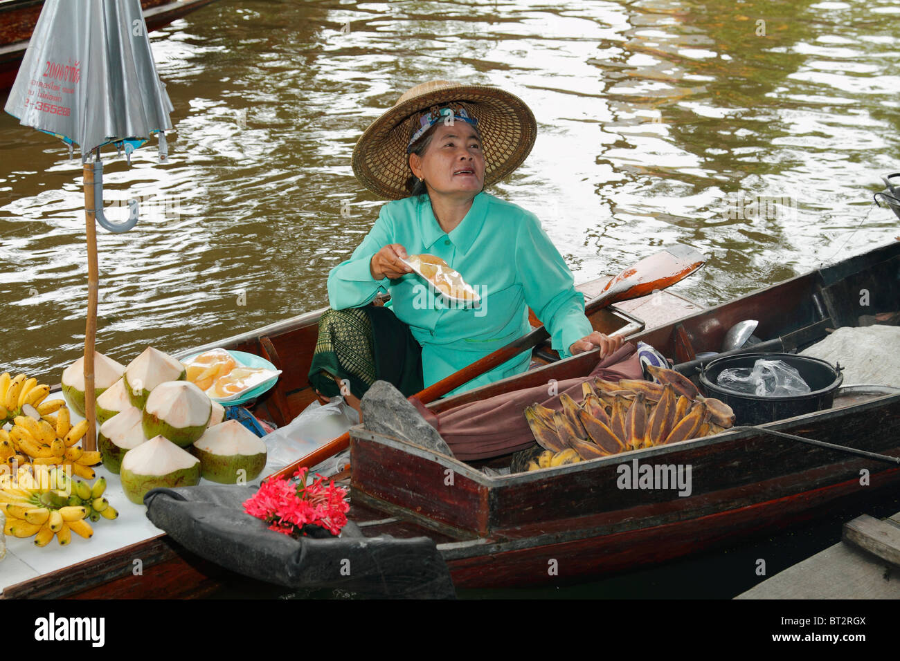 Anziana donna Thai venditore a vendere prodotti alimentari a sua barca a remi (barca a remi), al Mercato Galleggiante di Bangkok, Tailandia, Settembre 2010 Foto Stock
