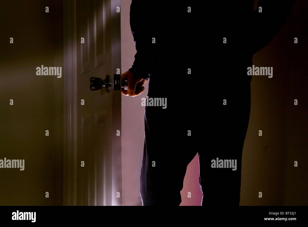 L'uomo ruotando la maniglia di apertura di una porta di entrare in una stanza buia Foto Stock