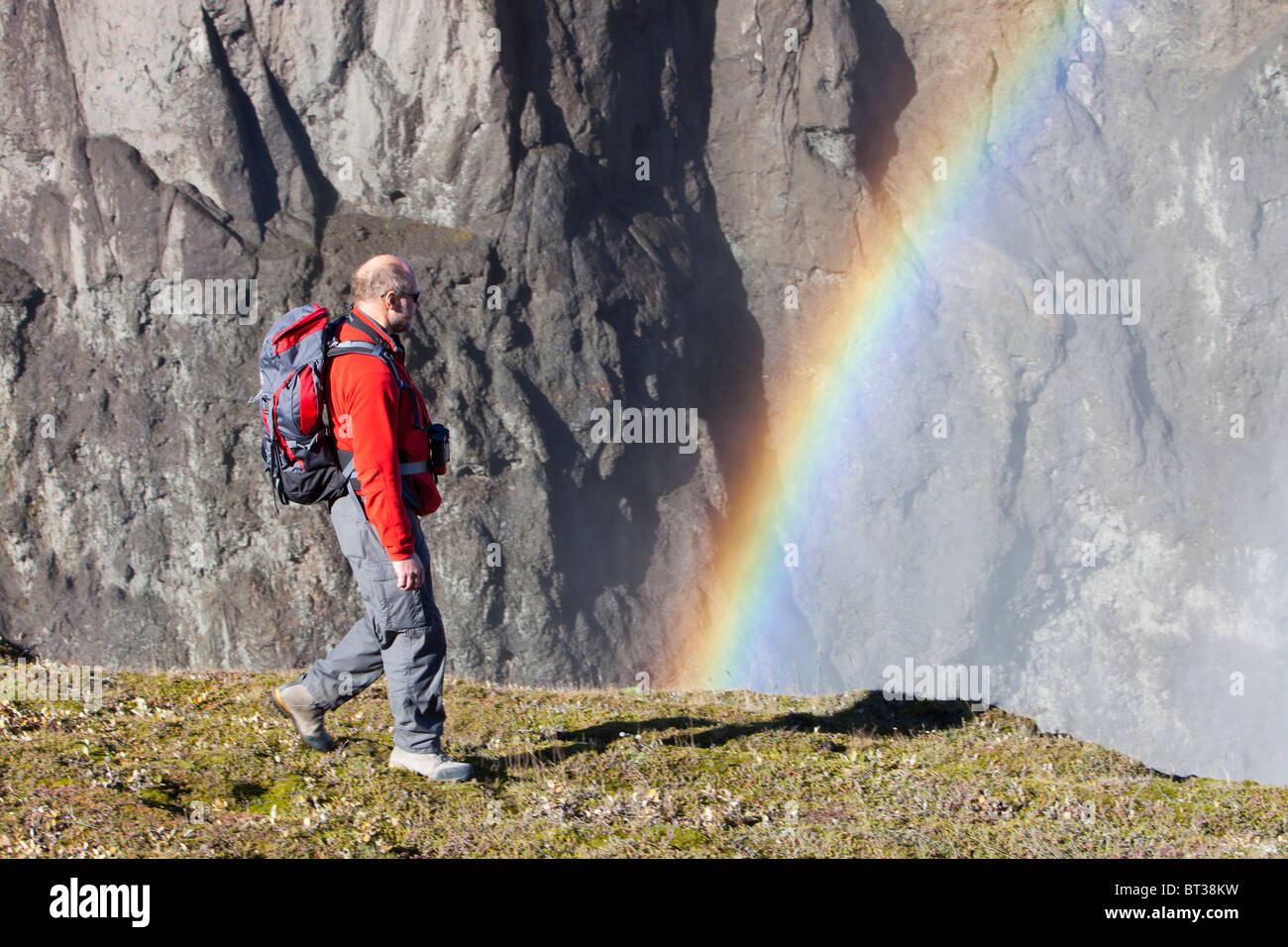 Un uomo cammina passato un arcobaleno in spray da oltre versare del Karahnjukar progetto idro, Islanda Foto Stock